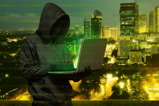 Hacker man with mask typing on laptop against modern city background