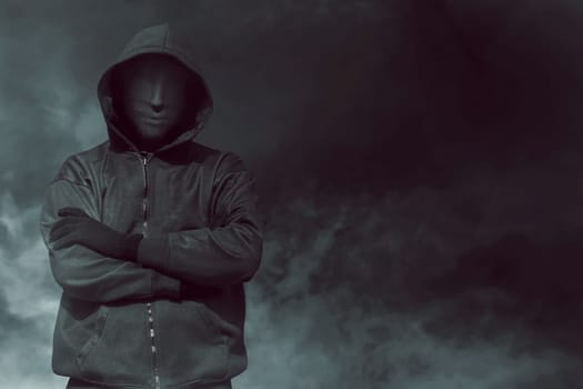 Hooded man with mask standing alone in the empty dark room