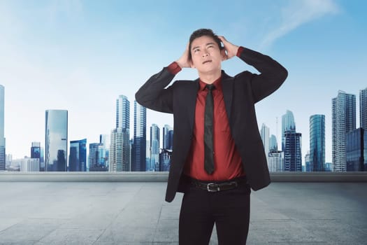 Young asian businessman suffering from headache against cityscape background
