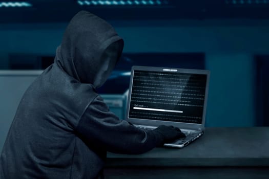 Hacker man wearing mask using laptop to upload computer virus in the office