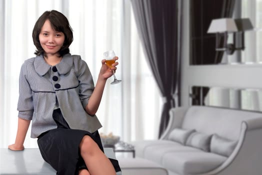 Relaxed asian woman sitting on desk with glass of wine at home