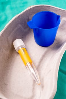 Medical test tube for urine samle lying in a one use capsule on the hospital's green background. The background can be a textile part of a doctor or nurse's work uniform