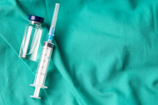 Medical syringe and vials lying on the hospital's green background. The background can be a textile part of a doctor or nurse's work uniform
