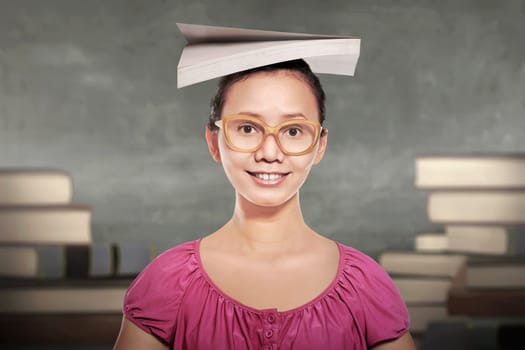 Young asian woman student in glasses with book on her head in the classroom