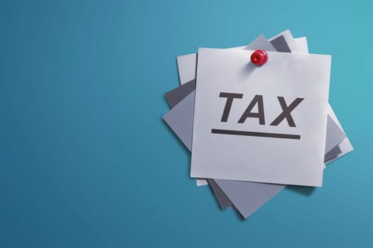 White note paper and written Tax for reminder on blue background