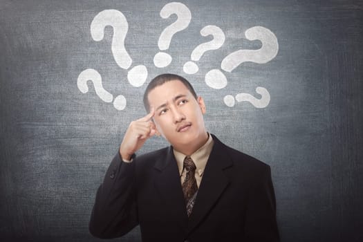 Young asian businessman confused with question marks above his head on black background