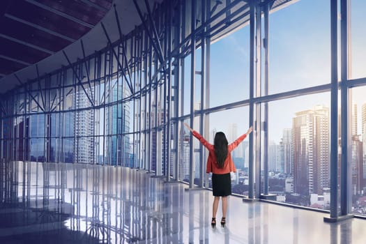 Happy asian business woman looking of skyscraper building from window