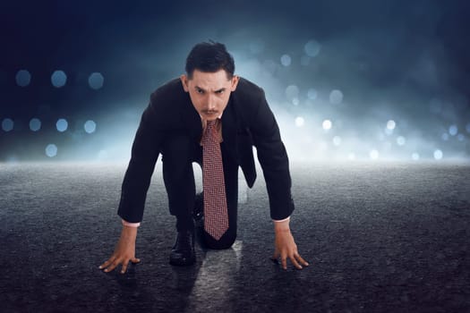 Young asian businessman in start position getting ready for run with concrete background