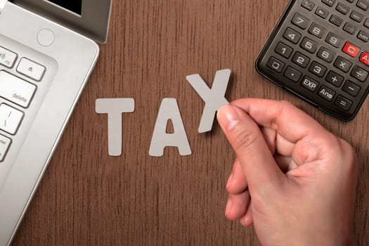 Hand holding Tax words on table with laptop and calculator on wooden table