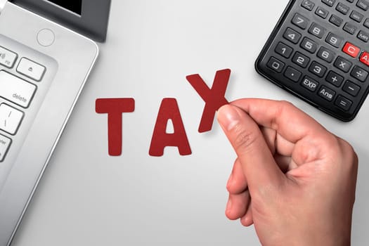 Hand holding Tax text on table with laptop and calculator on white board