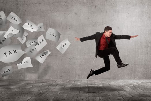 Young asian businessman run away from flying paper with Tax text on the street