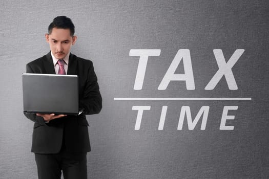 Young asian businessman working on laptop with TAX TIME text on the wall