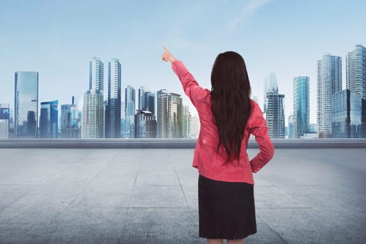 Attractive Asian business woman pointing something empty space on cityscape background