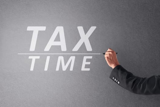 Business person hand writing Tax Time with pen on blackboard