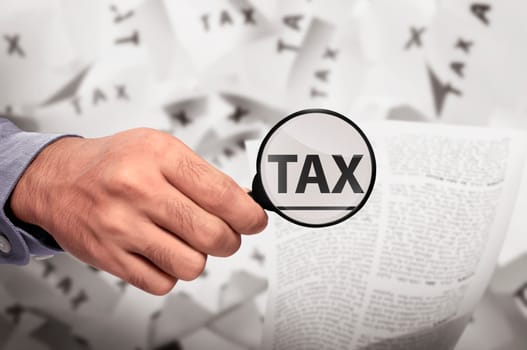 Business hand looking Tax word using magnifying glass on the paper