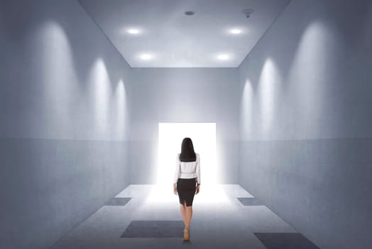 Back view of a young asian business woman walking to opened door in the office