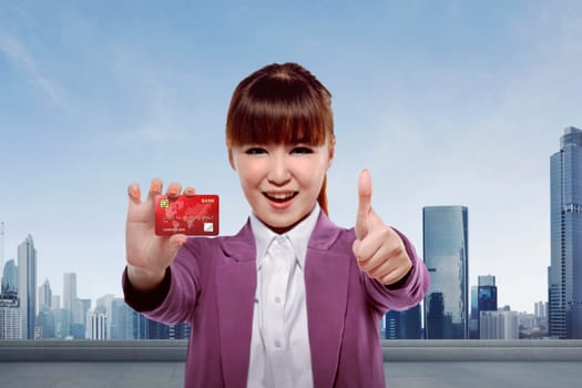 Young asian business woman showing credit card against cityscape background