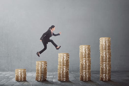 Young asian business woman climb up the gold coins on a grey background