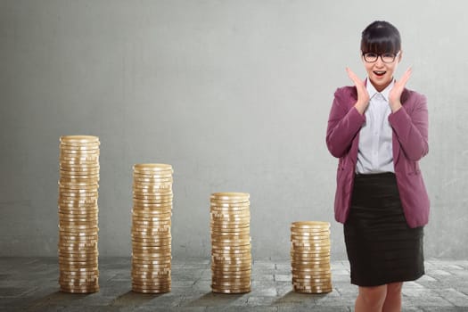 Beautiful asian business woman standing with golden stack coins over grey background