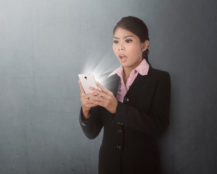 Young asian business woman using smartphone with shocked expression on the grey wall