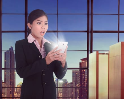 Beautiful asian business woman using smartphone with surprised expression in the workplace