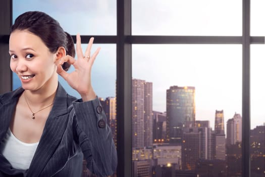 Happy asian businesswoman showing okay gesture against cityscape background