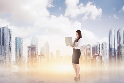 Attractive asian business woman using a laptop while standing against cityscape background