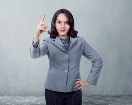 Asian business woman pointing something over gray wall background