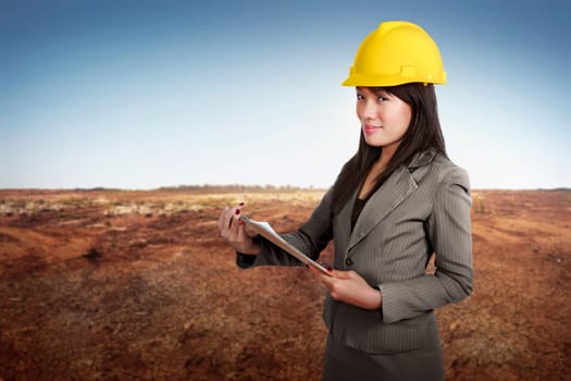 Happy asian contractor woman holding blueprint on clipboard at construction site