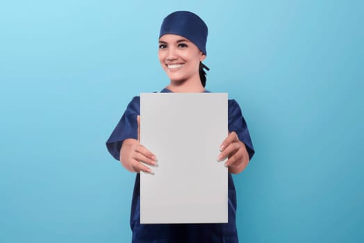 Smiling asian woman nurse showing blank paper over blue background