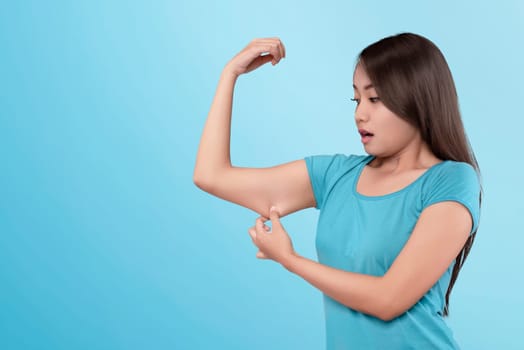 Young asian woman losing muscle on her arm on blue background