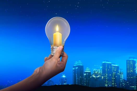 People hand holding candles light inside light bulb with modern city background