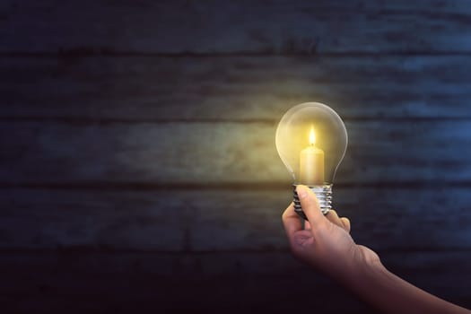 People hand holding bright candle inside light bulb on the dark room