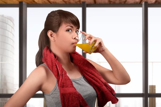 Sporty asian woman drink orange juice glass with glasses window background