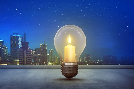 Burning candle inside light bulb on floor with modern city background