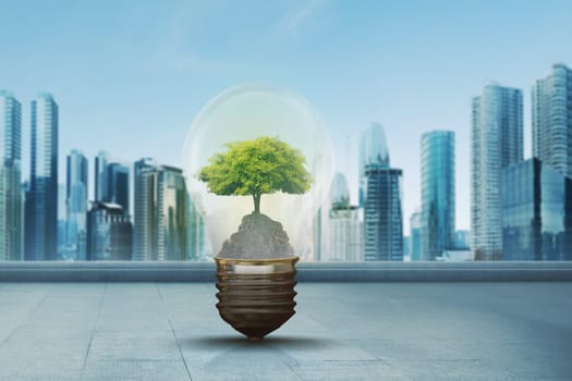 Green tree inside light bulb against modern city background