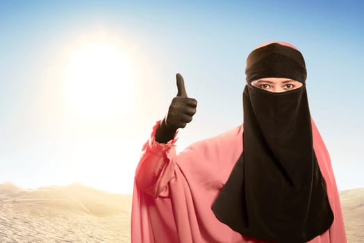 Cheerful asian muslim woman wearing hijab with good sign against sunlight background