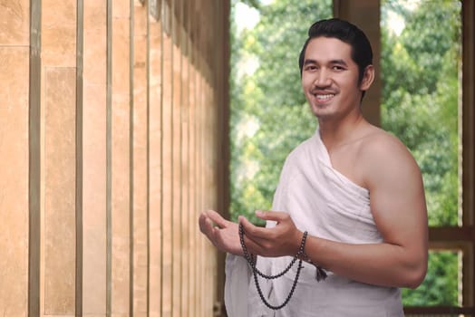 Handsome asian muslim male with ihram holding prayer beads on the mosque