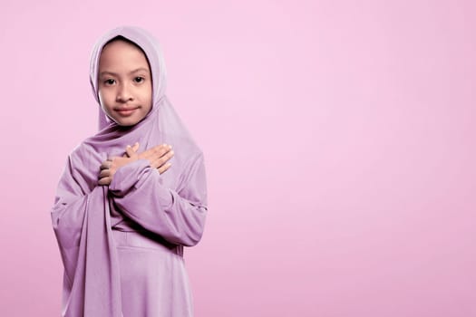 Small asian muslim girl in hijab with peaceful expression over pink background