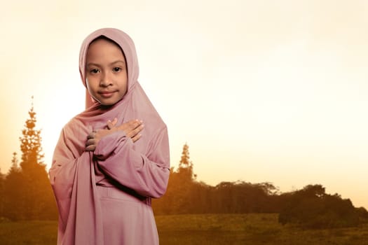 Portrait of asian muslim child wearing veil standing on the field at sunset