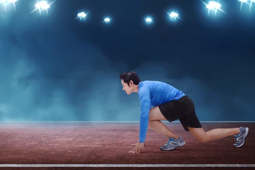 Young asian runner man kneeling ready in start position on race track