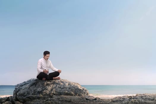 Handsome asian muslim man praying with prayer beads on the beach