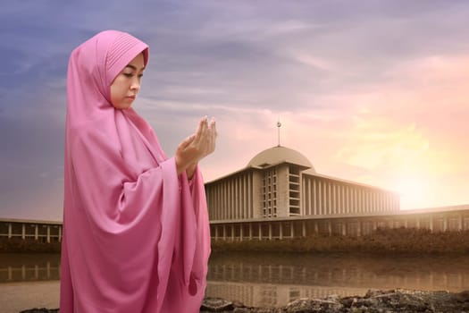 Portrait of asian muslim woman in hijab praying with mosque background