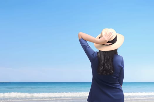 Happy asian woman holding her hat and enjoying trip on the beach