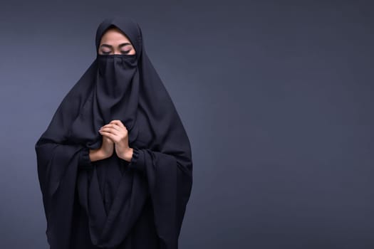 Young asian muslim woman wearing niqab praying with dark background