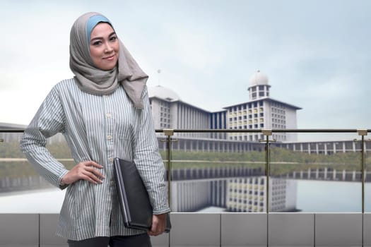 Portrait of asian muslim woman with hijab holding laptop with mosque background