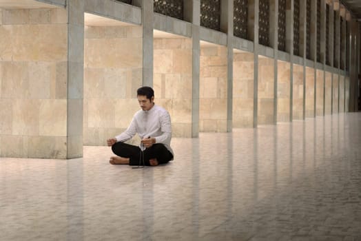 Religious asian muslim man with prayer beads praying in the mosque