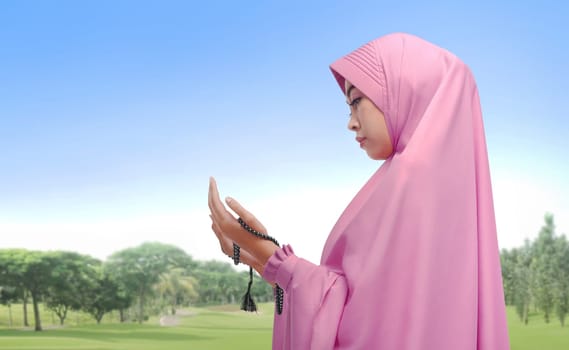 Beautiful asian muslim woman praying with prayer beads at outdoor