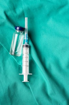 Medical syringe and vials lying on the hospital's green background. The background can be a textile part of a doctor or nurse's work uniform