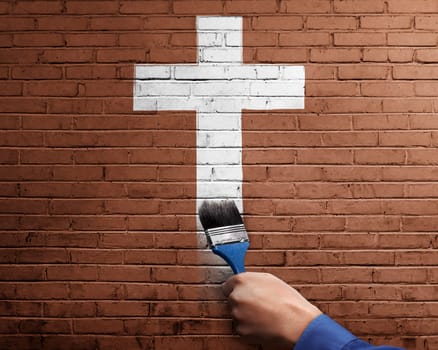 People hand with paint brush making white cross shape on brick wall